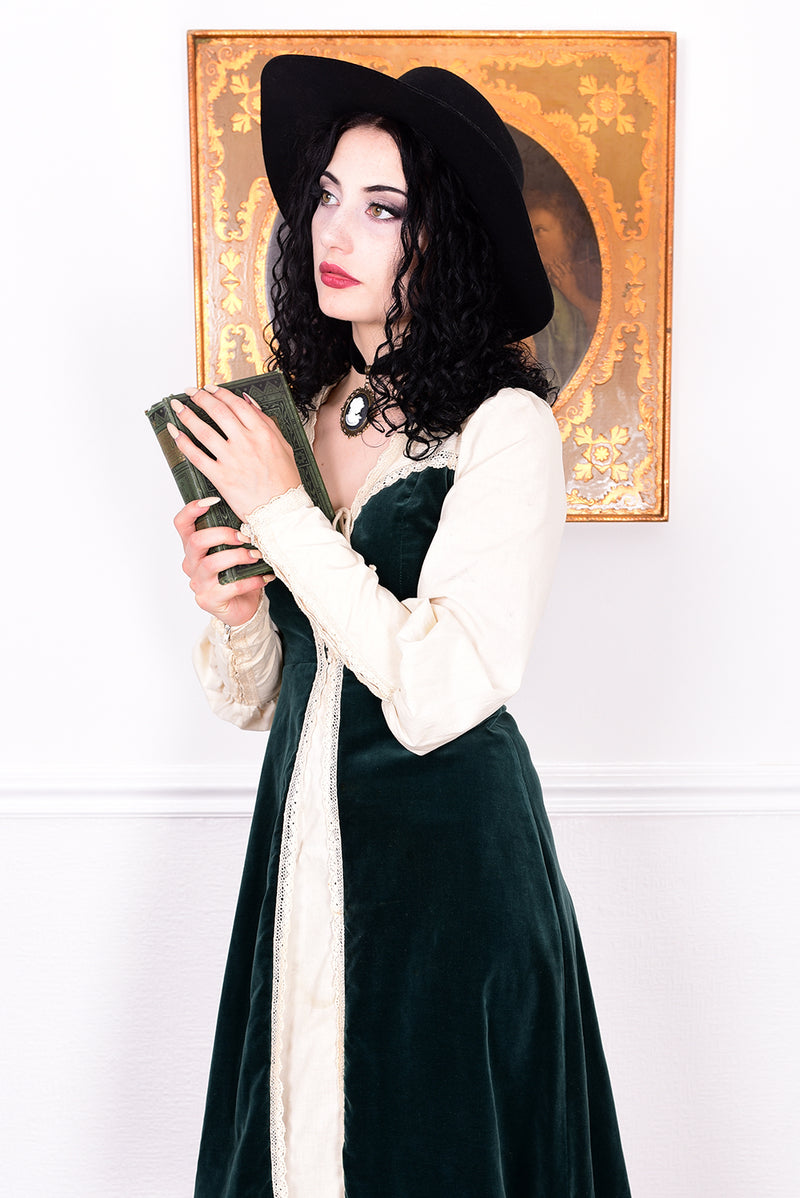 Woman in a vintage 1970s Gunne Sax green velvet dress with white lace details standing against a white wall.