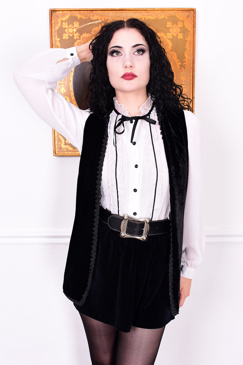 Woman wearing a black vest over a white shirt with a bow tie, standing against a white background.