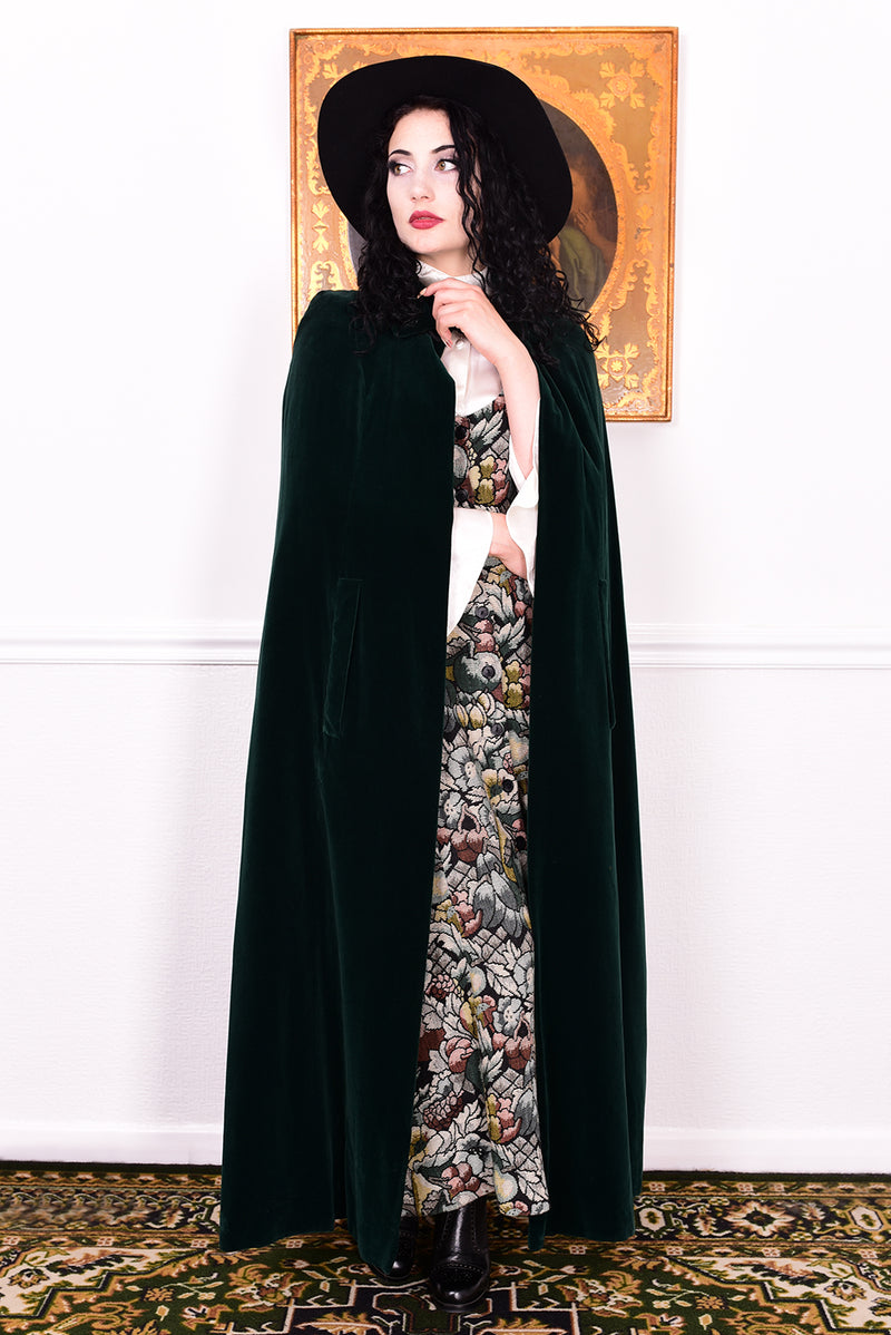 Woman wearing a vintage 1970s green velvet cape by Quad standing in a room with a white wall.