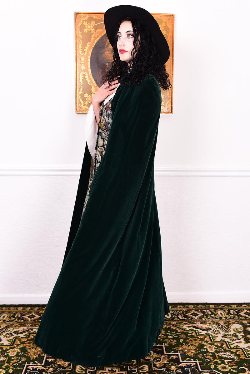 Woman wearing a vintage 1970s green velvet cape by Quad standing in a room with a white wall.