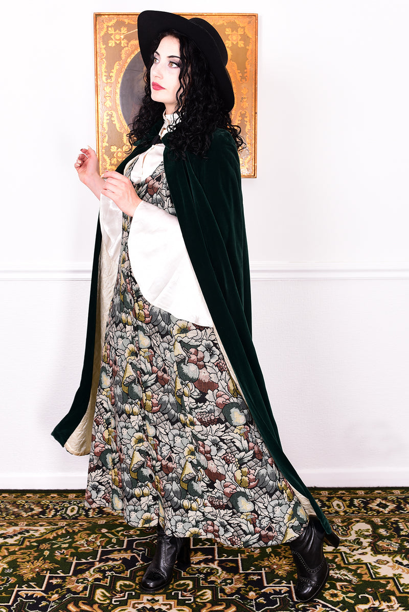 Woman wearing a vintage 1970s green velvet cape by Quad standing in a room with a white wall.