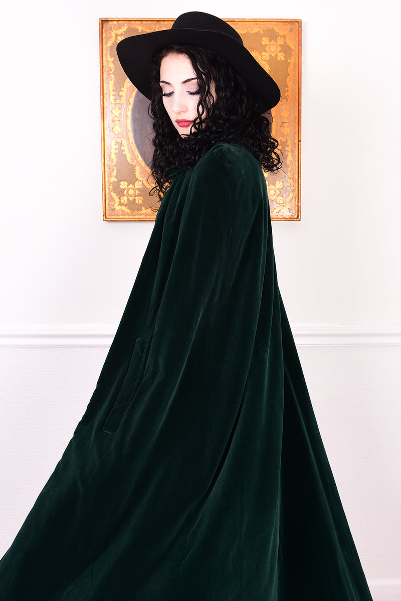 Woman wearing a vintage 1970s green velvet cape by Quad standing in a room with a white wall.