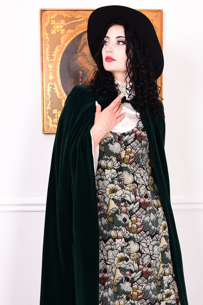 Woman wearing a vintage 1970s green velvet cape by Quad standing in a room with a white wall.