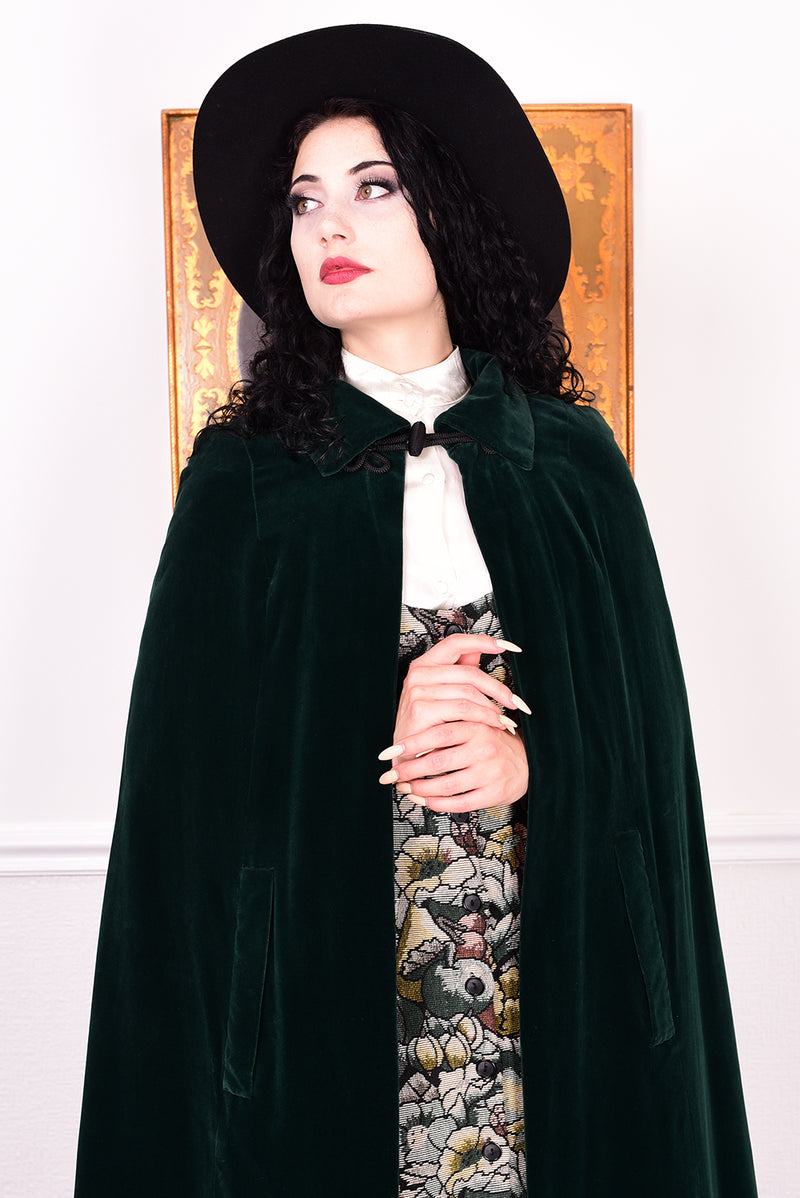 Woman wearing a vintage 1970s green velvet cape by Quad standing in a room with a white wall.