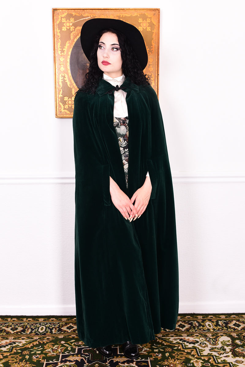 Woman wearing a vintage 1970s green velvet cape by Quad standing in a room with a white wall.
