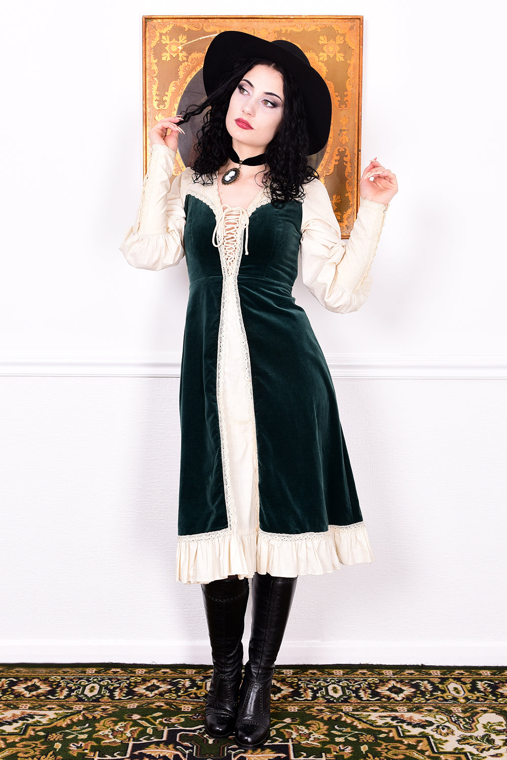 Woman in a vintage 1970s Gunne Sax green velvet dress with white lace details  standing against a white wall.
