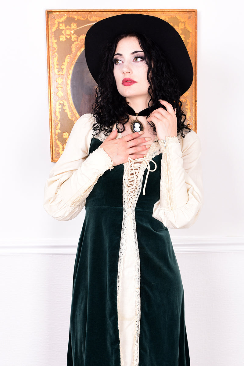 Woman in a vintage 1970s Gunne Sax green velvet dress with white lace details  standing against a white wall.