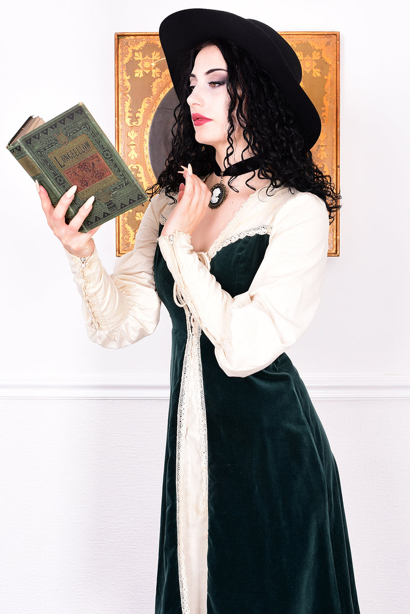 Woman in a vintage 1970s Gunne Sax green velvet dress with white lace details  standing against a white wall.