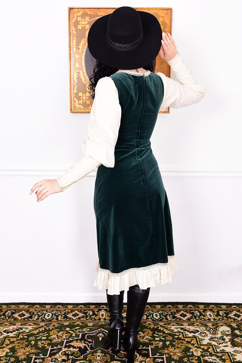 Woman in a vintage 1970s Gunne Sax green velvet dress with white lace details  standing against a white wall.