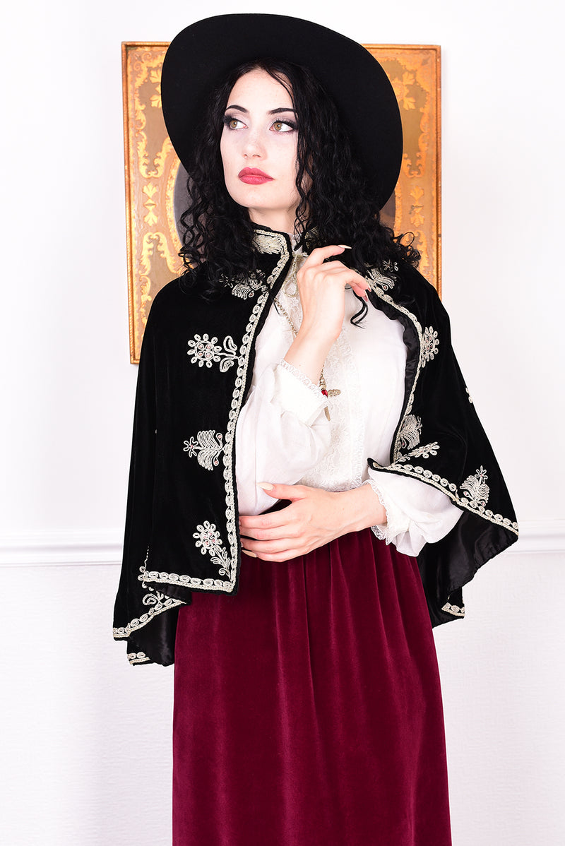 Woman wearing an antique early 1900s black embroidered cape over a dress.