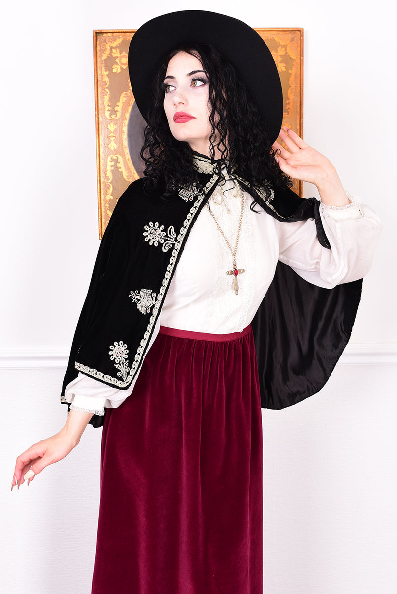 Woman wearing an antique early 1900s black embroidered cape over a dress.