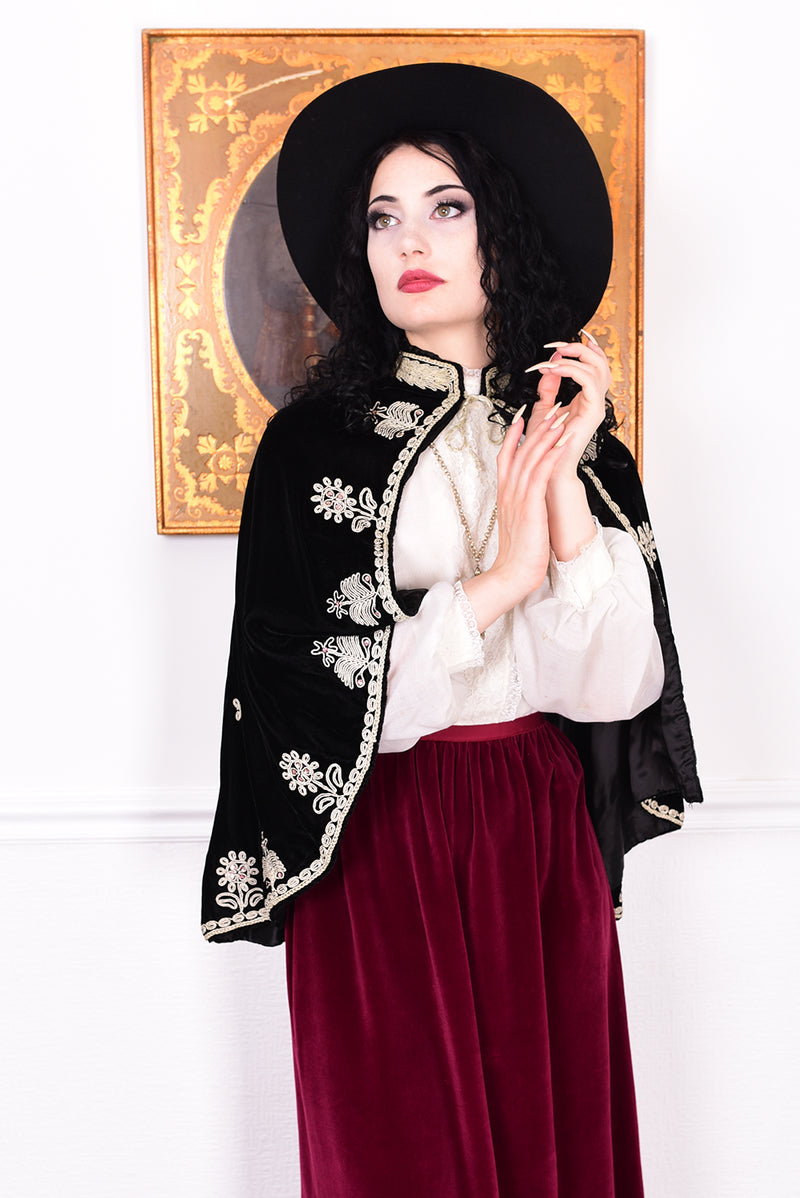 Woman wearing an antique early 1900s black embroidered cape over a dress.