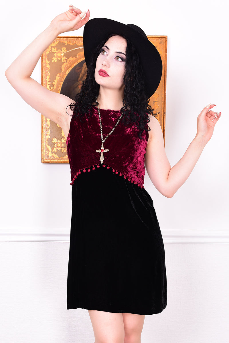 Woman wearing a black and red velvet vintage 1960s dress against a white wall.