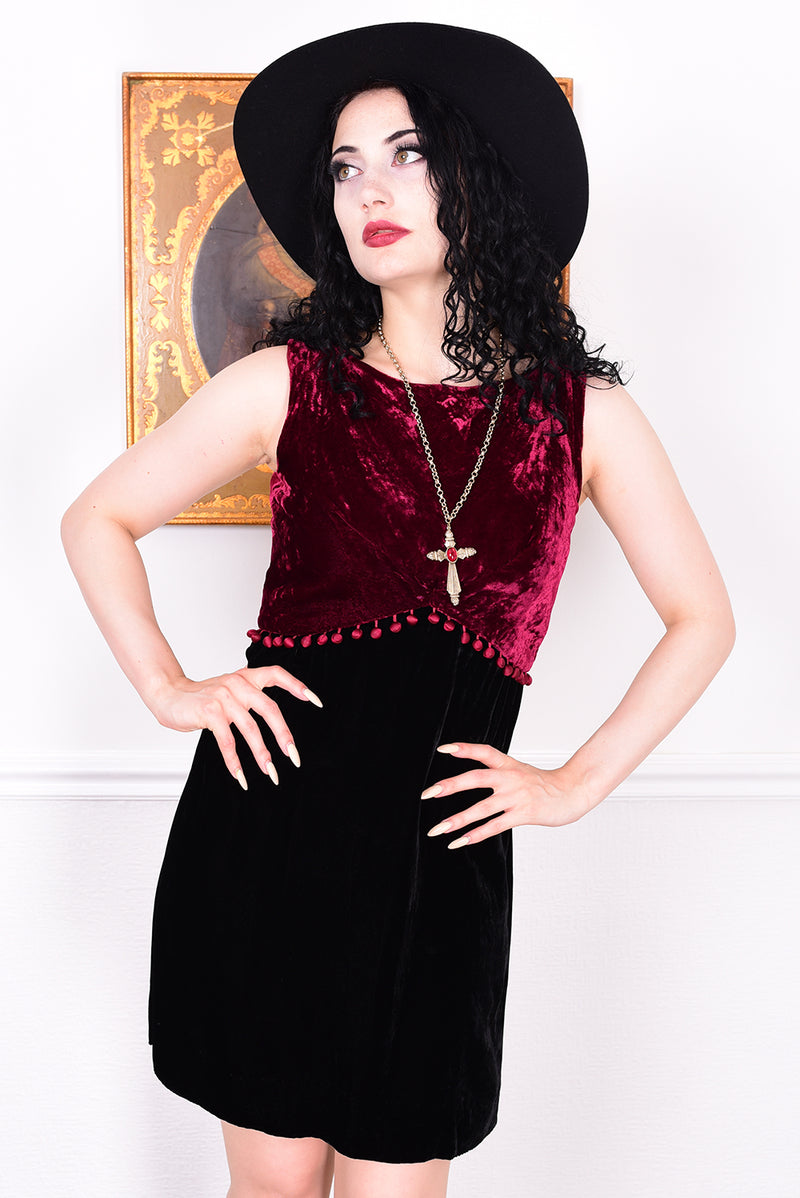 Woman wearing a black and red velvet vintage 1960s dress against a white wall.