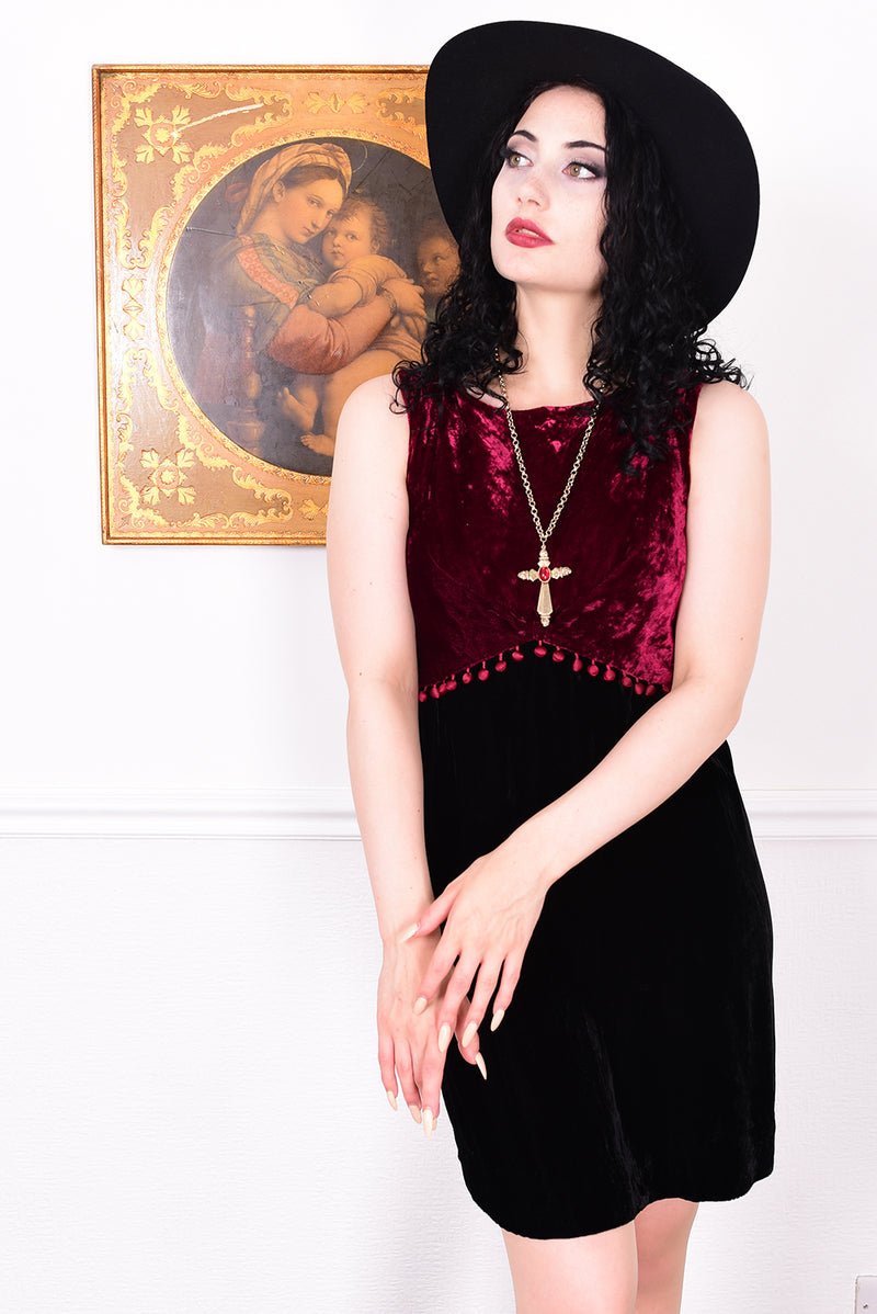 Woman wearing a black and red velvet vintage 1960s dress against a white wall.