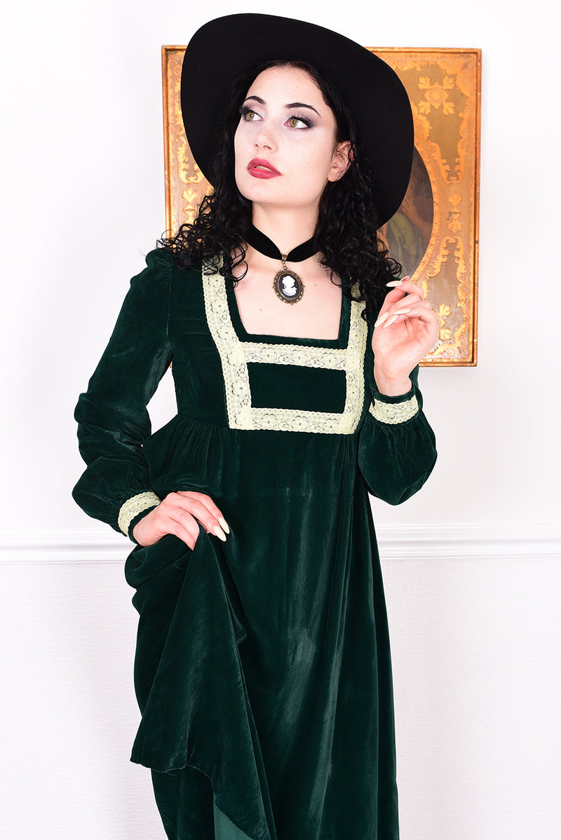 Woman in a vintage 1970s emerald green velvet dress with white lace trim standing against a white wall.