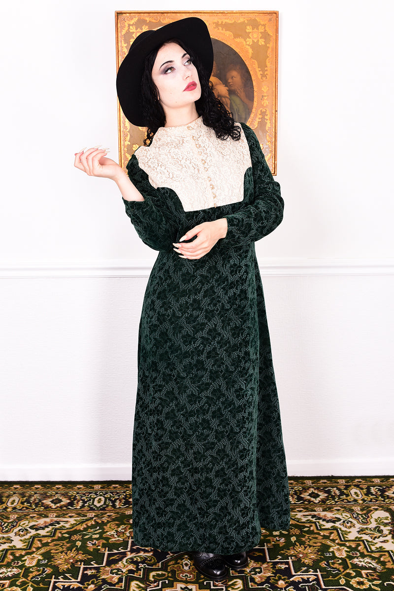 Woman in a vintage 1970s dark green floral print velvet maxi dress with lace details and a black hat.