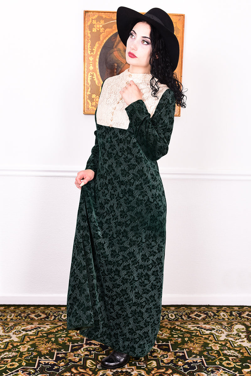 Woman in a vintage 1970s dark green floral print velvet maxi dress with lace details and a black hat.