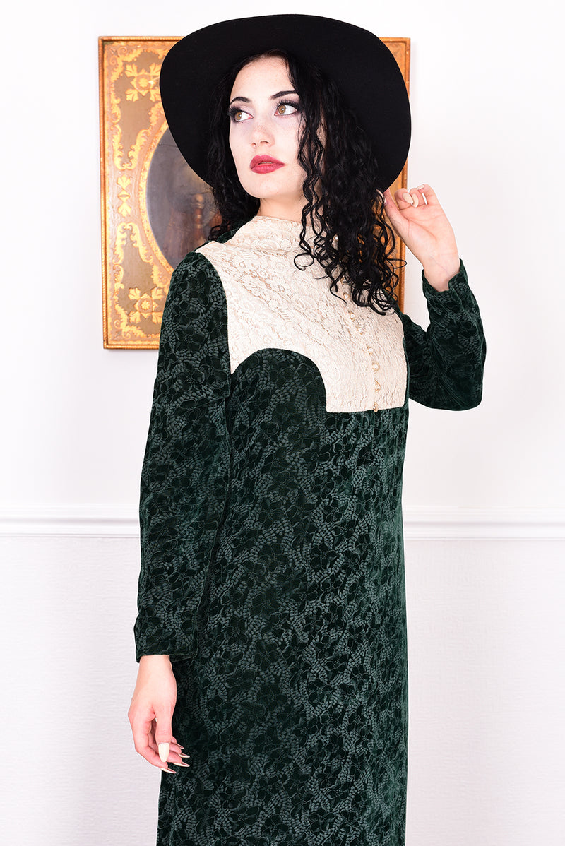 Woman in a vintage 1970s dark green floral print velvet maxi dress with lace details and a black hat.