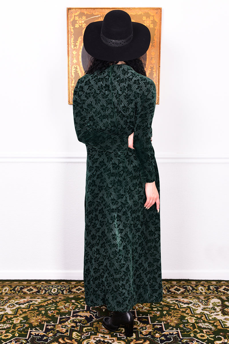 Woman in a vintage 1970s dark green floral print velvet maxi dress with lace details and a black hat.