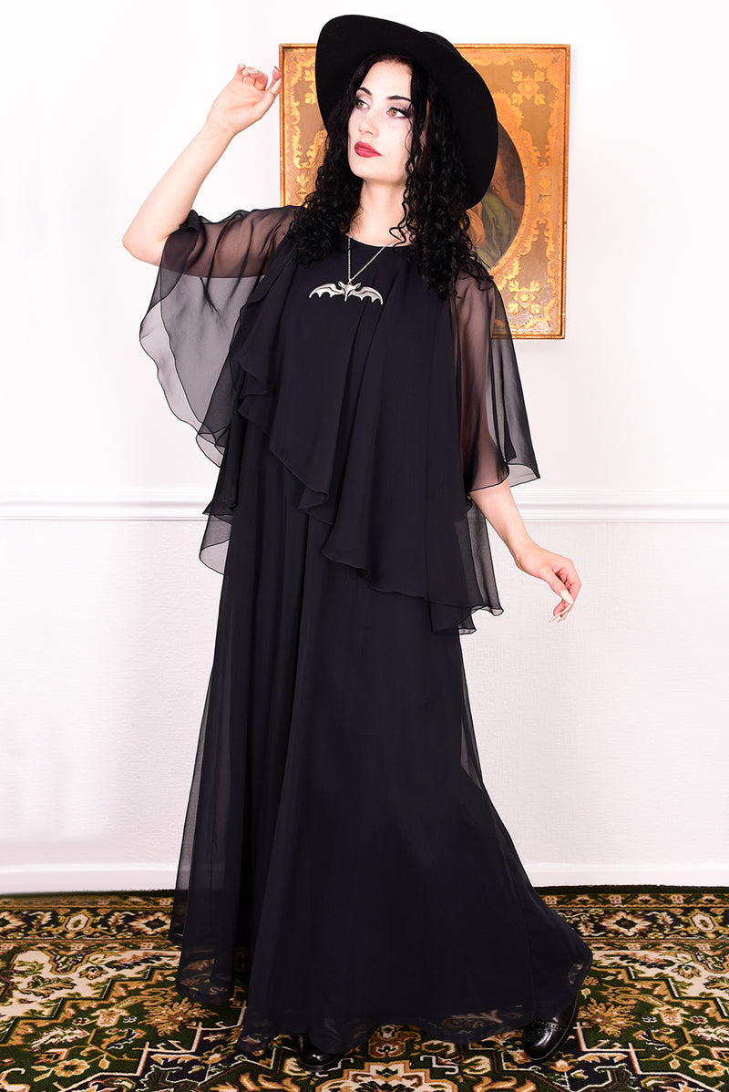 Woman wearing a black vintage 1970s floaty dress with sheer sleeves.