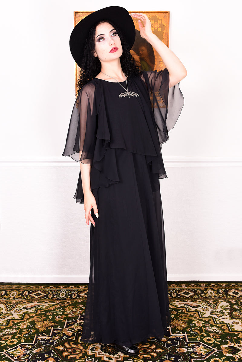 Woman wearing a black vintage 1970s floaty dress with sheer sleeves.