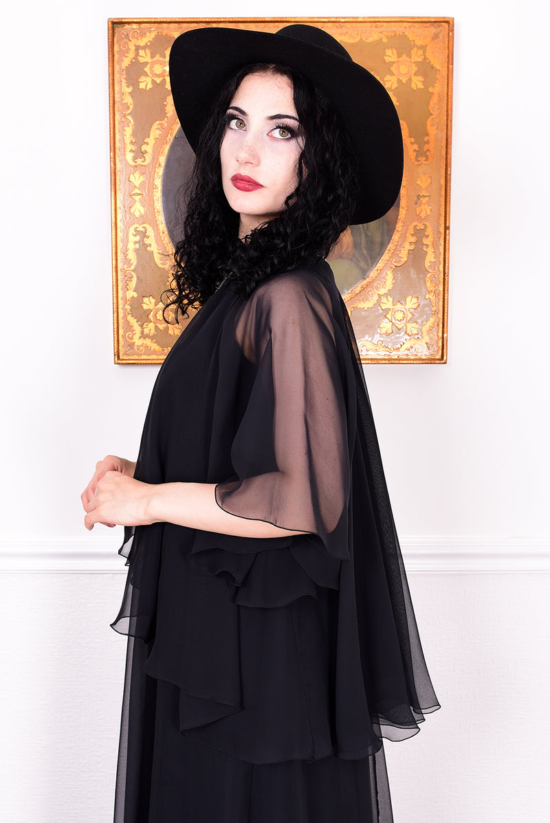 Woman wearing a black vintage 1970s floaty dress with sheer sleeves.