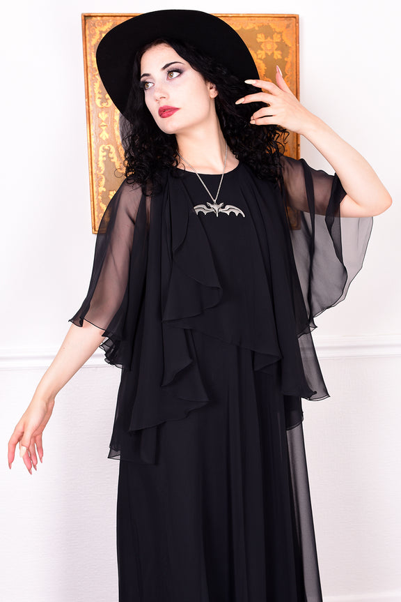 Woman wearing a black vintage 1970s floaty dress with sheer sleeves.
