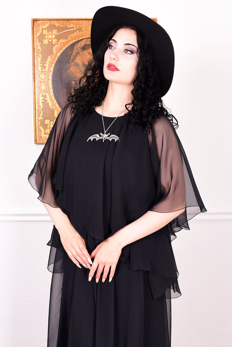 Woman wearing a black vintage 1970s floaty dress with sheer sleeves.