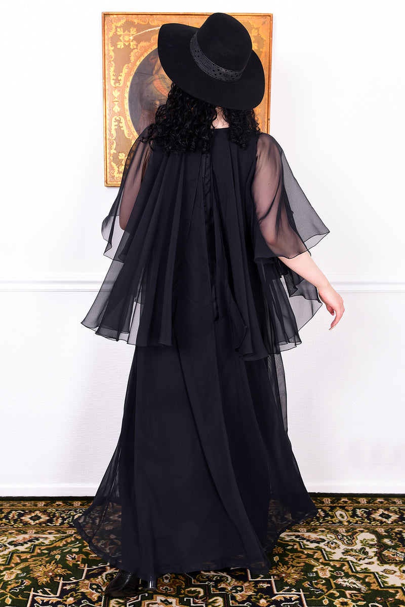 Woman wearing a black vintage 1970s floaty dress with sheer sleeves.