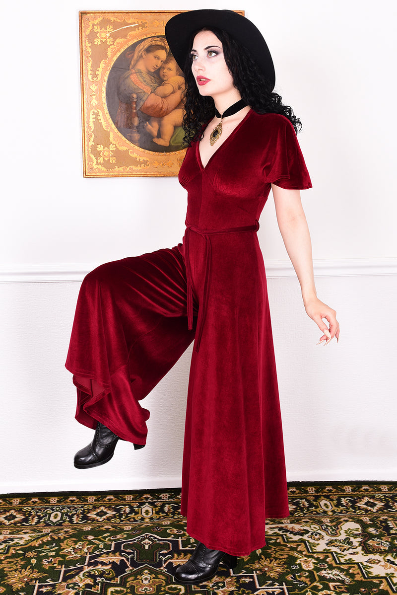 Woman in a red vintage velvet jumpsuit standing in a room with a painting on the wall.