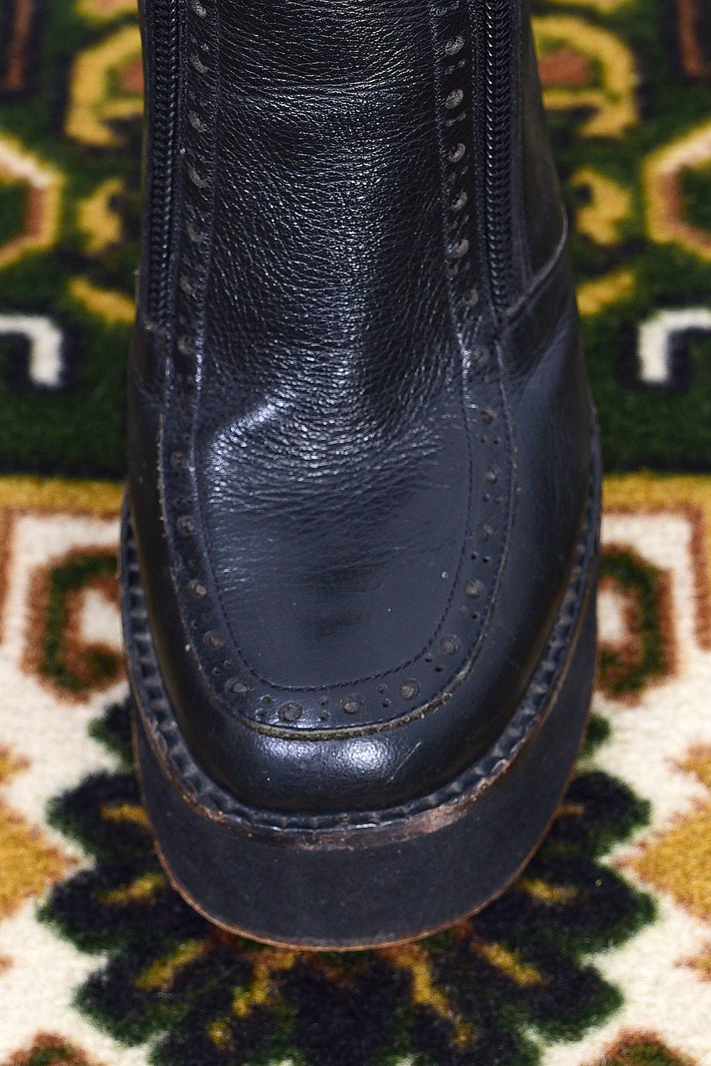Pair of black vintage 1990s platform boots on a patterned rug with a white wall background.