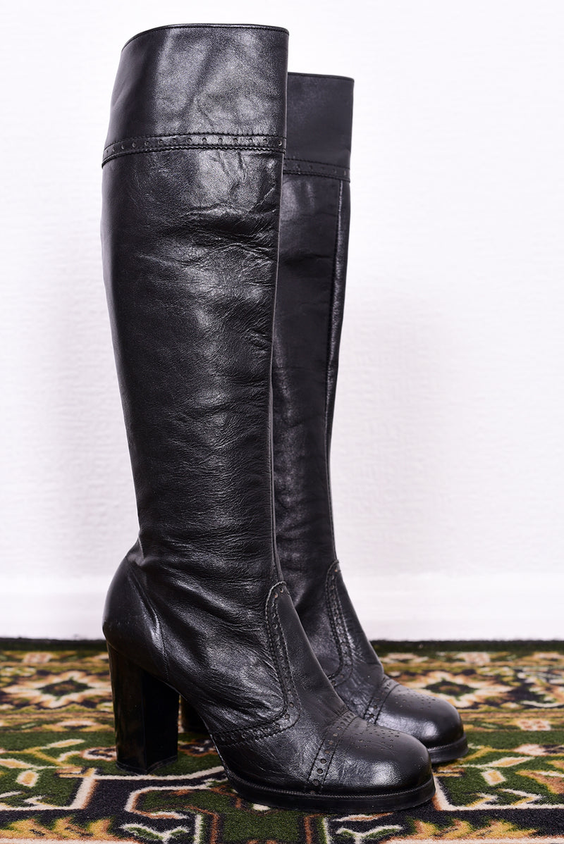 Pair of vintage 1970s black knee-high boots on a patterned rug.