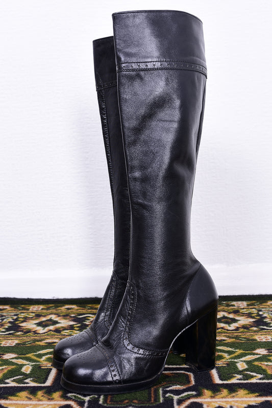 Pair of vintage 1970s black knee-high boots on a patterned rug.