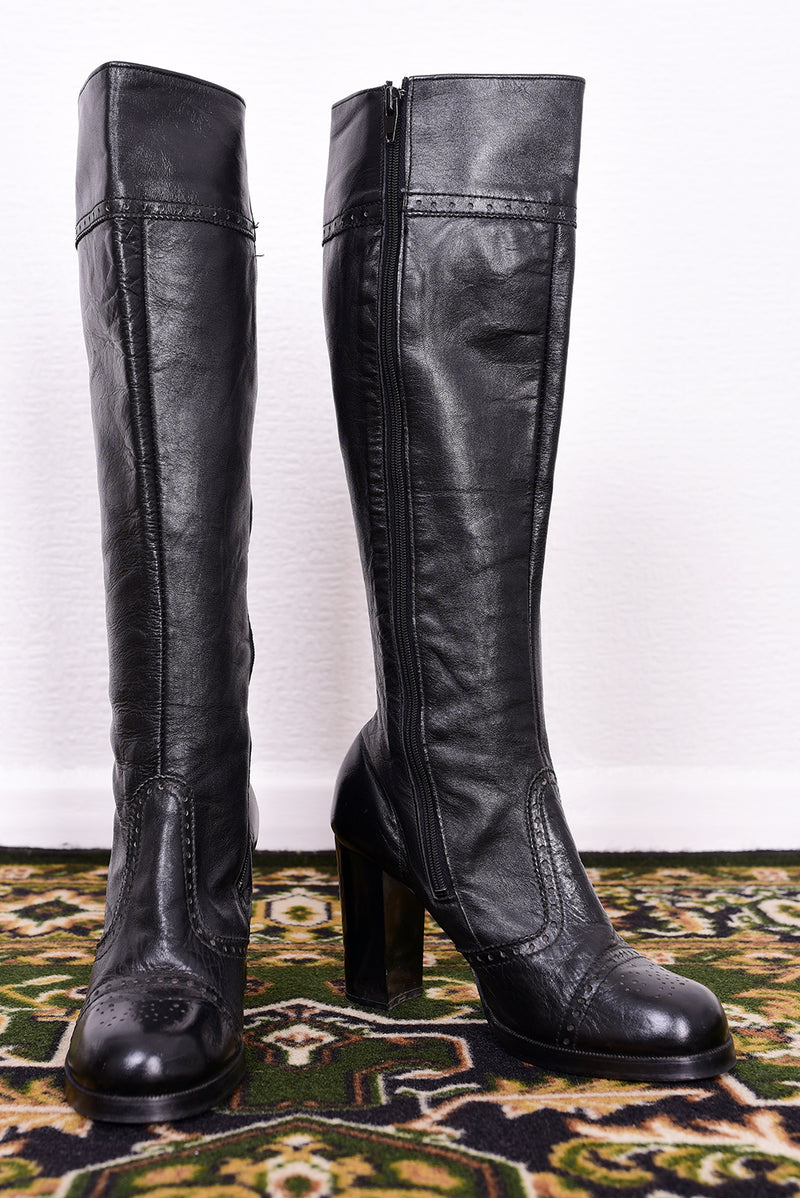Pair of vintage 1970s black knee-high boots on a patterned rug.