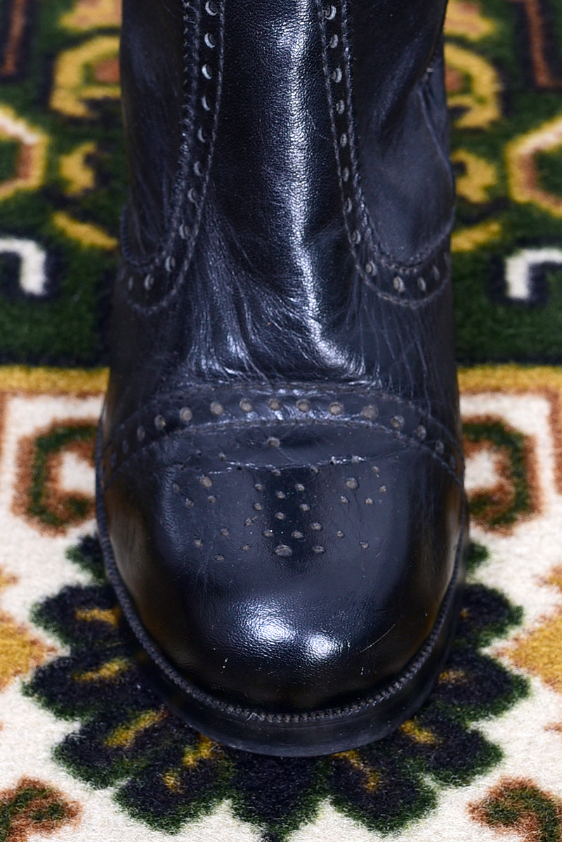 Pair of vintage 1970s black knee-high boots on a patterned rug.