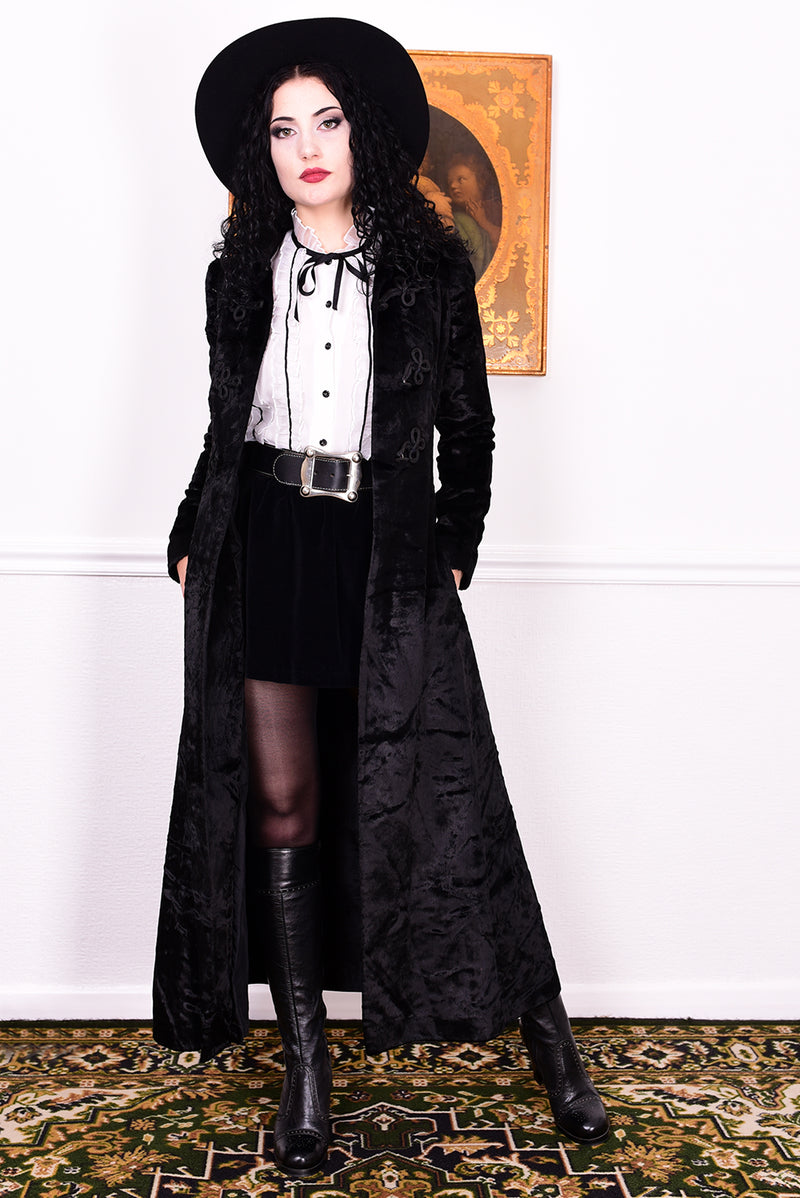 Woman wearing a vintage 1970s long black plush coat and hat against a white wall.