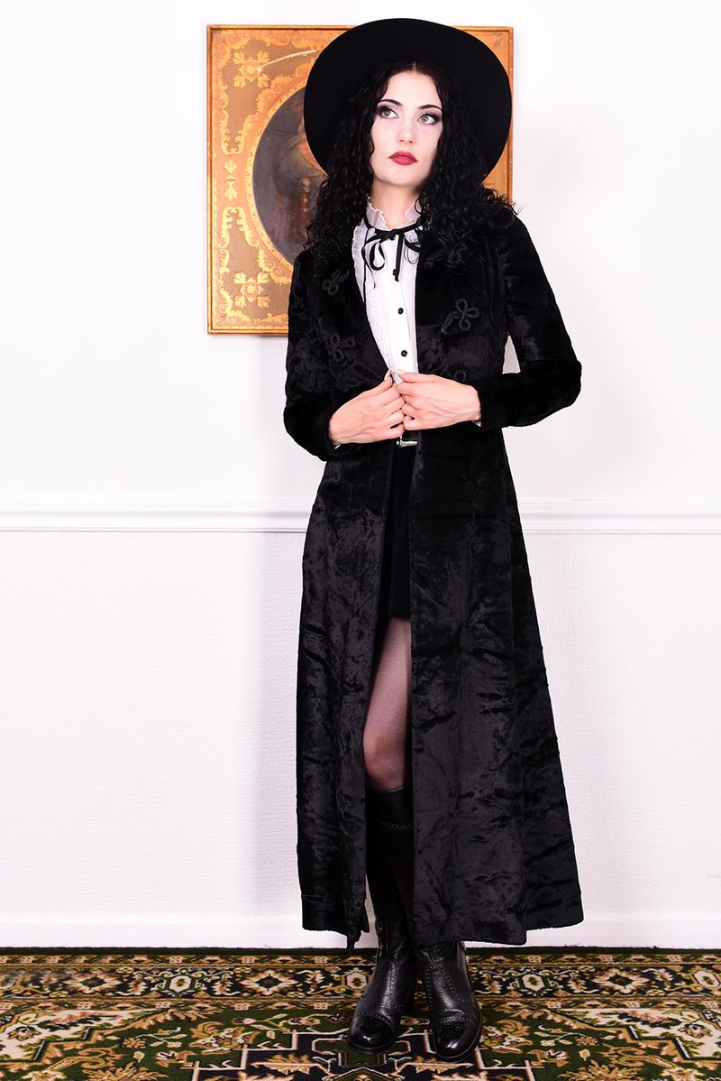 Woman wearing a vintage 1970s long black plush coat and hat against a white wall.