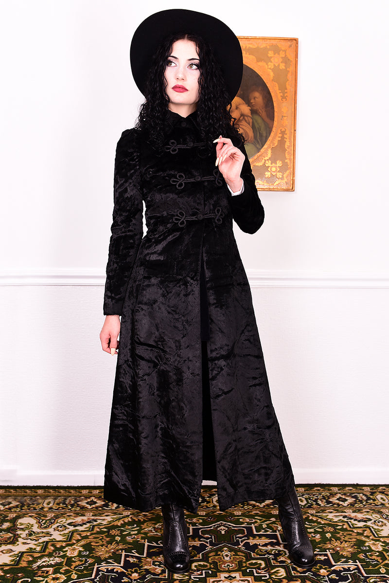 Woman wearing a vintage 1970s long black plush coat and hat against a white wall.