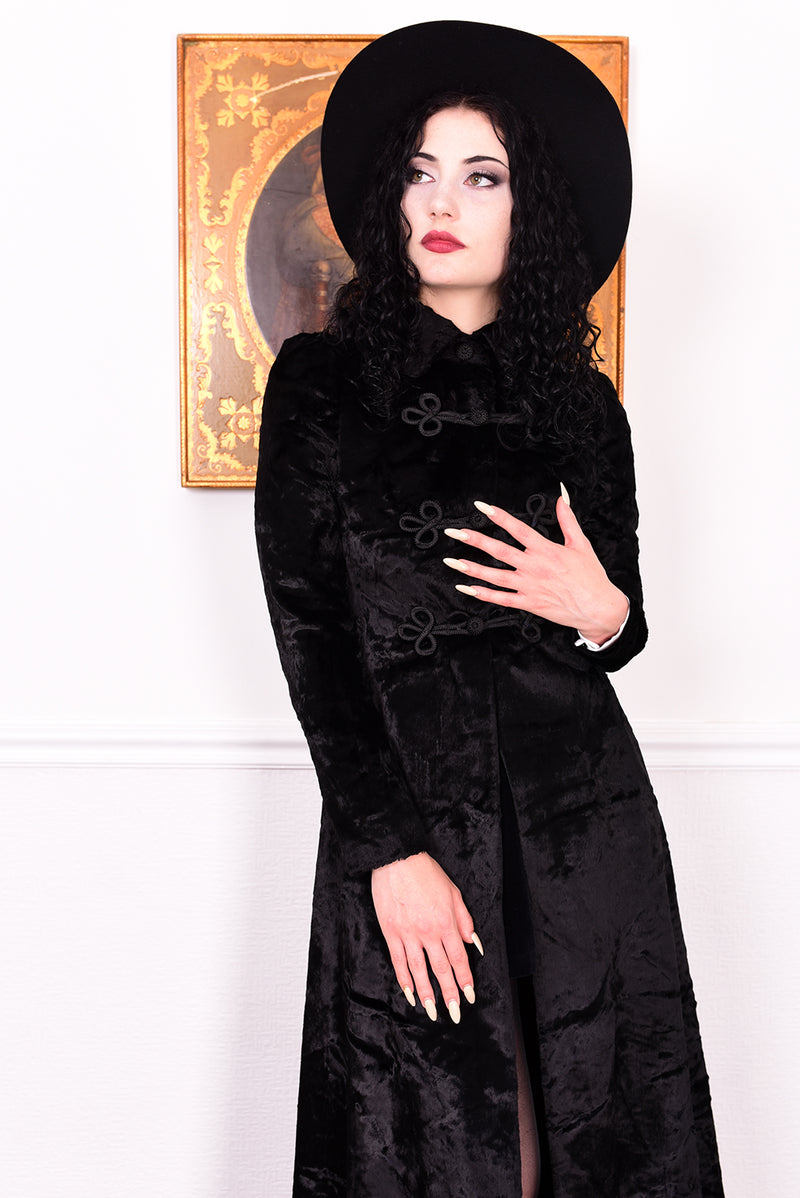 Woman wearing a vintage 1970s long black plush coat and hat against a white wall.