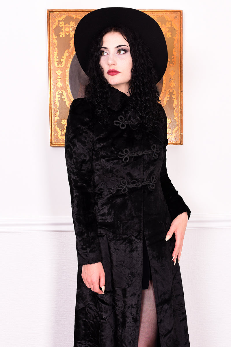 Woman wearing a vintage 1970s long black plush coat and hat against a white wall.
