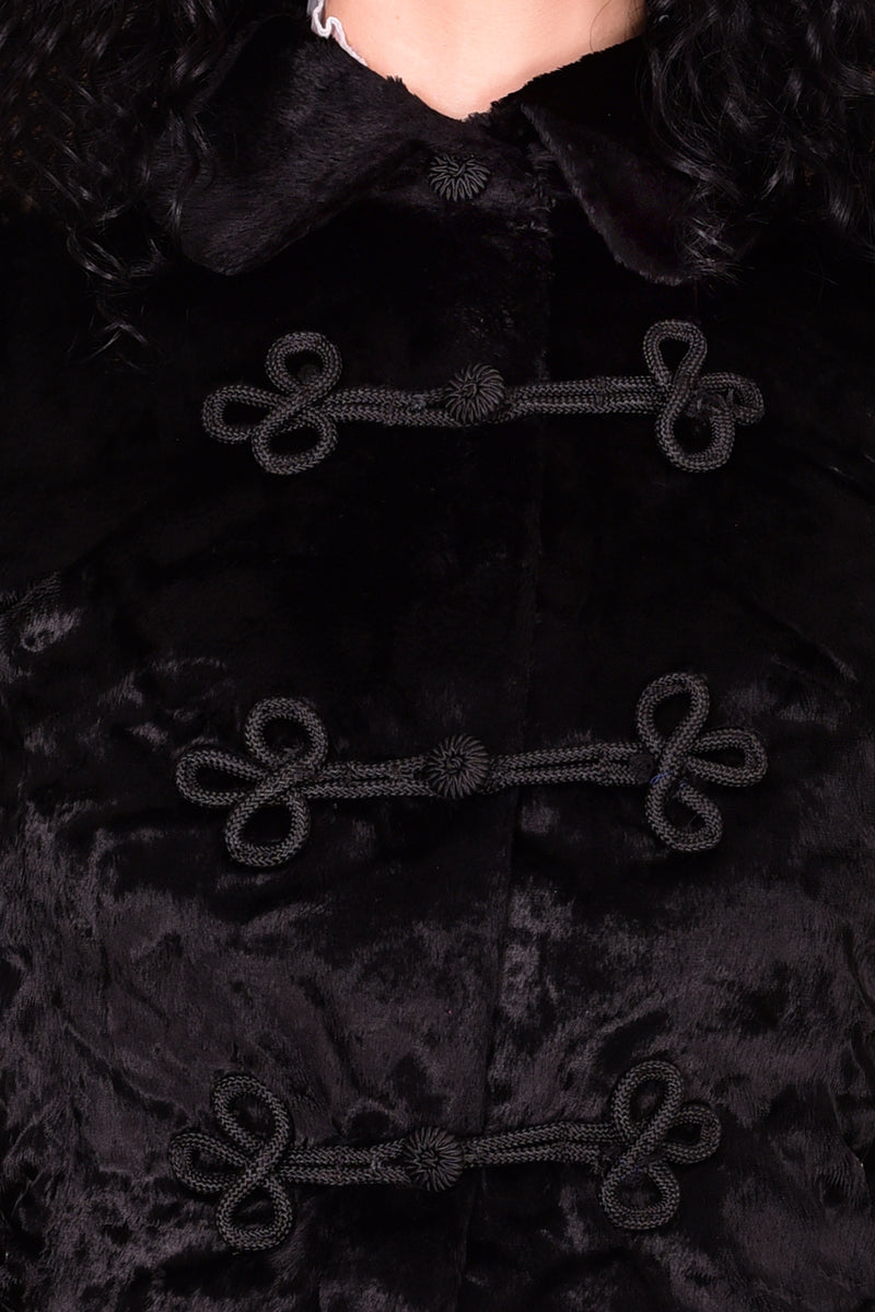 Woman wearing a vintage 1970s long black plush coat and hat against a white wall.