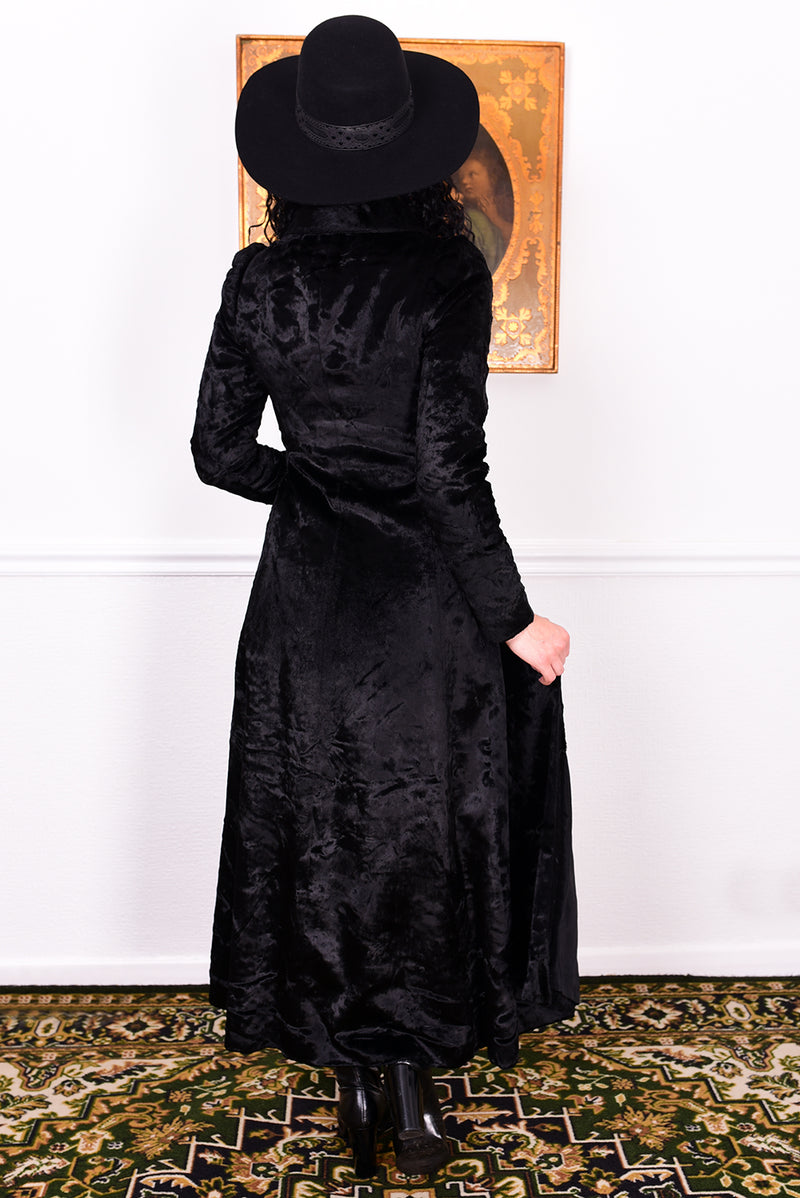 Woman wearing a vintage 1970s long black plush coat and hat against a white wall.