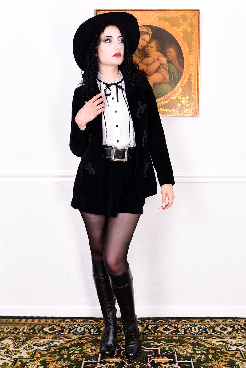 Woman wearing a vintage 1970s black velvet jacket with frog closures in front of a white wall.