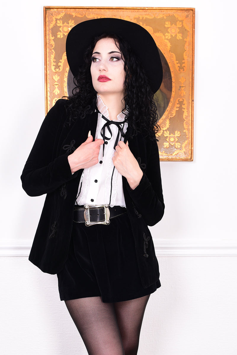 Woman wearing a vintage 1970s black velvet jacket with frog closures in front of a white wall.