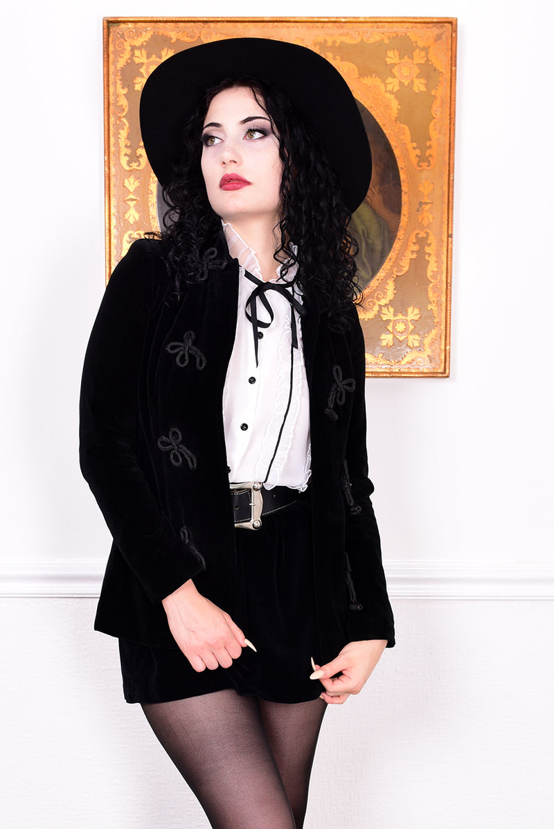 Woman wearing a vintage 1970s black velvet jacket with frog closures in front of a white wall.