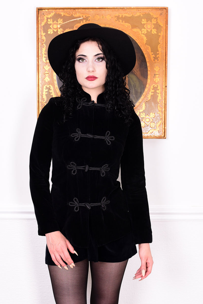 Woman wearing a vintage 1970s black velvet jacket with frog closures in front of a white wall.